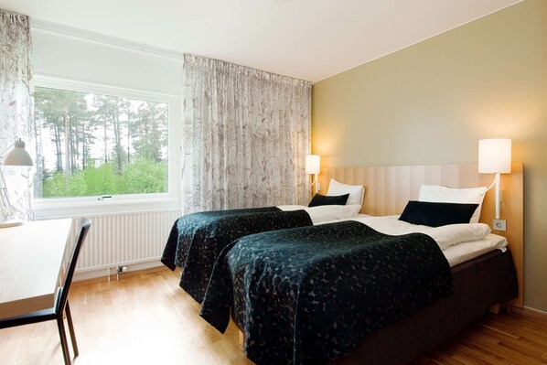 A hotel room with two beds, a window with curtains, a desk, and a chair.