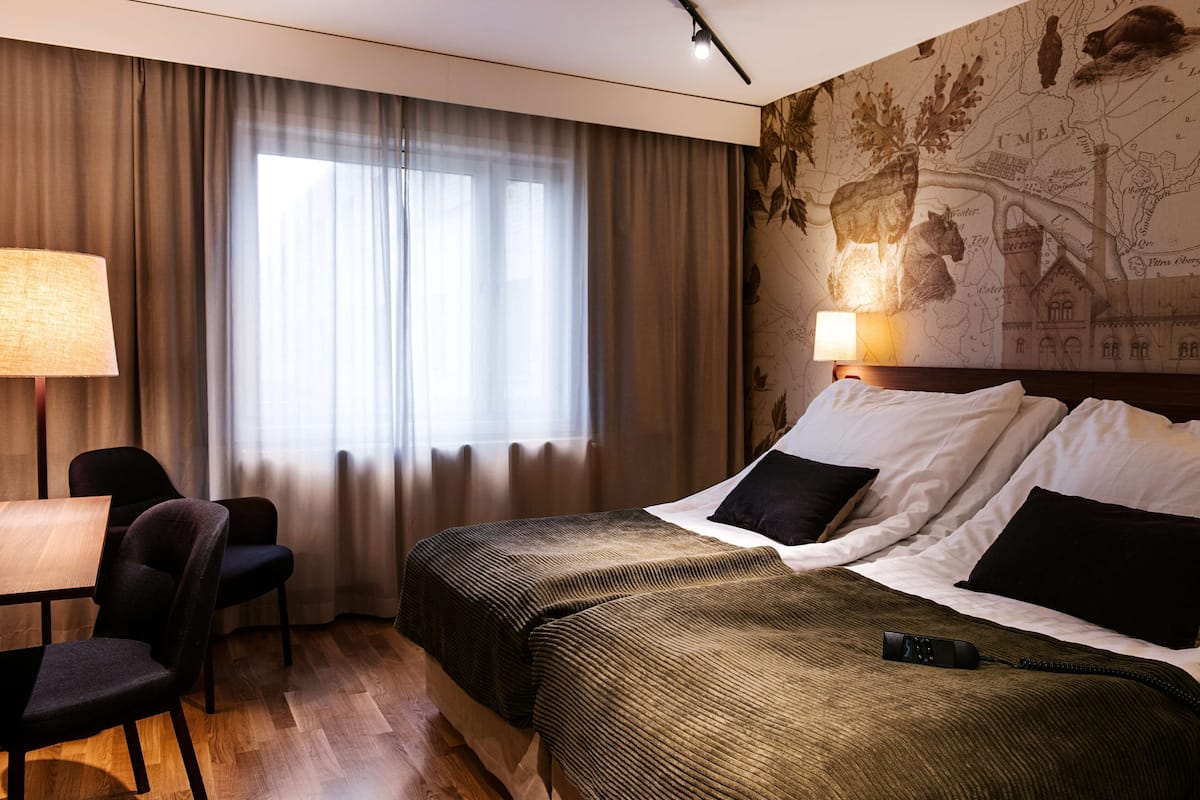 A hotel room with a bed, a desk, a chair, and a map on the wall.
