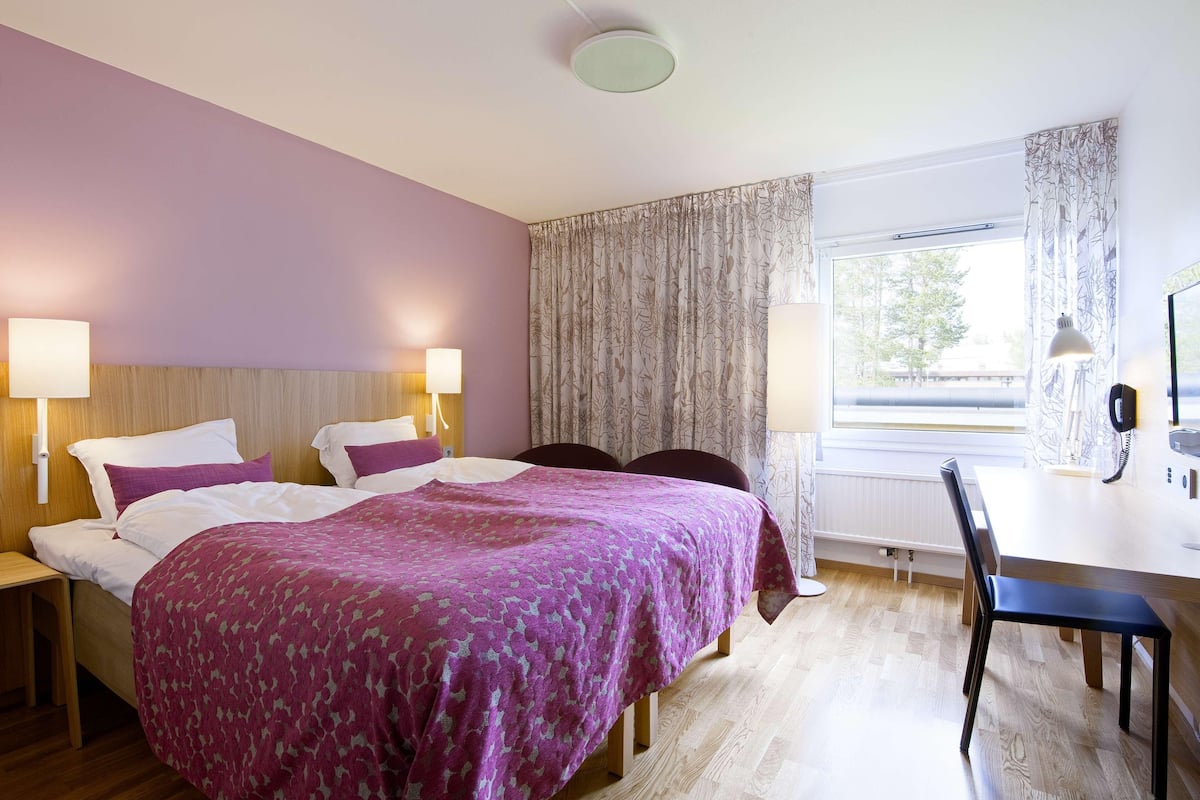 A hotel room with a bed, bedside lamps, a desk, and a chair.