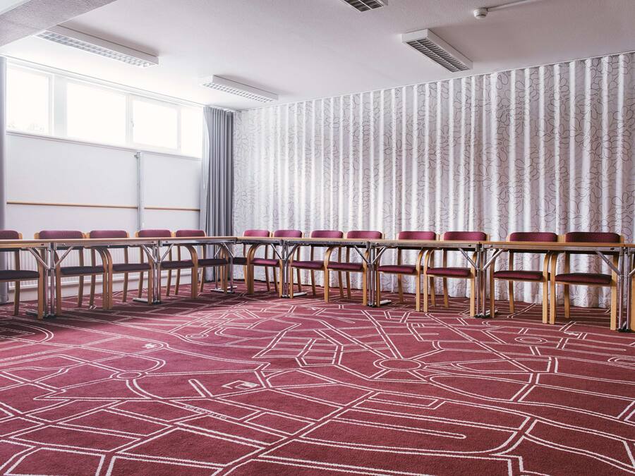 Sala de conferências com uma mesa comprida, cadeiras e um tapete estampado.