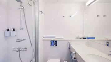 Ein modernes Badezimmer mit Duschkabine aus Glas, Toilette, Waschbecken mit Spiegel und Handtuchhalter.