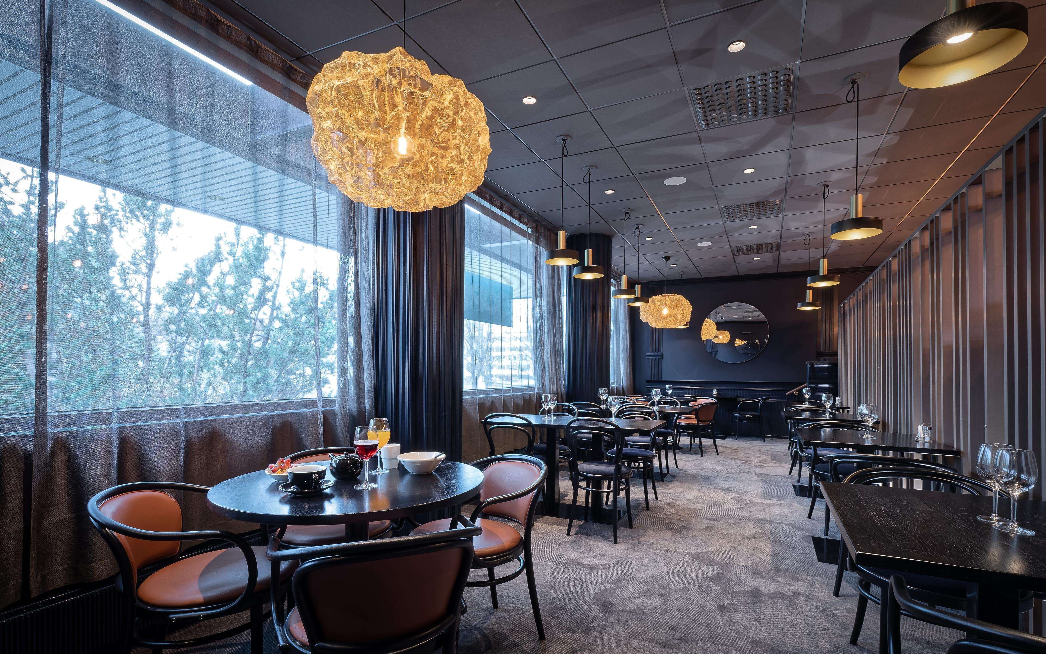 Un restaurante moderno con mesas redondas, sillas negras y lámparas colgantes originales.