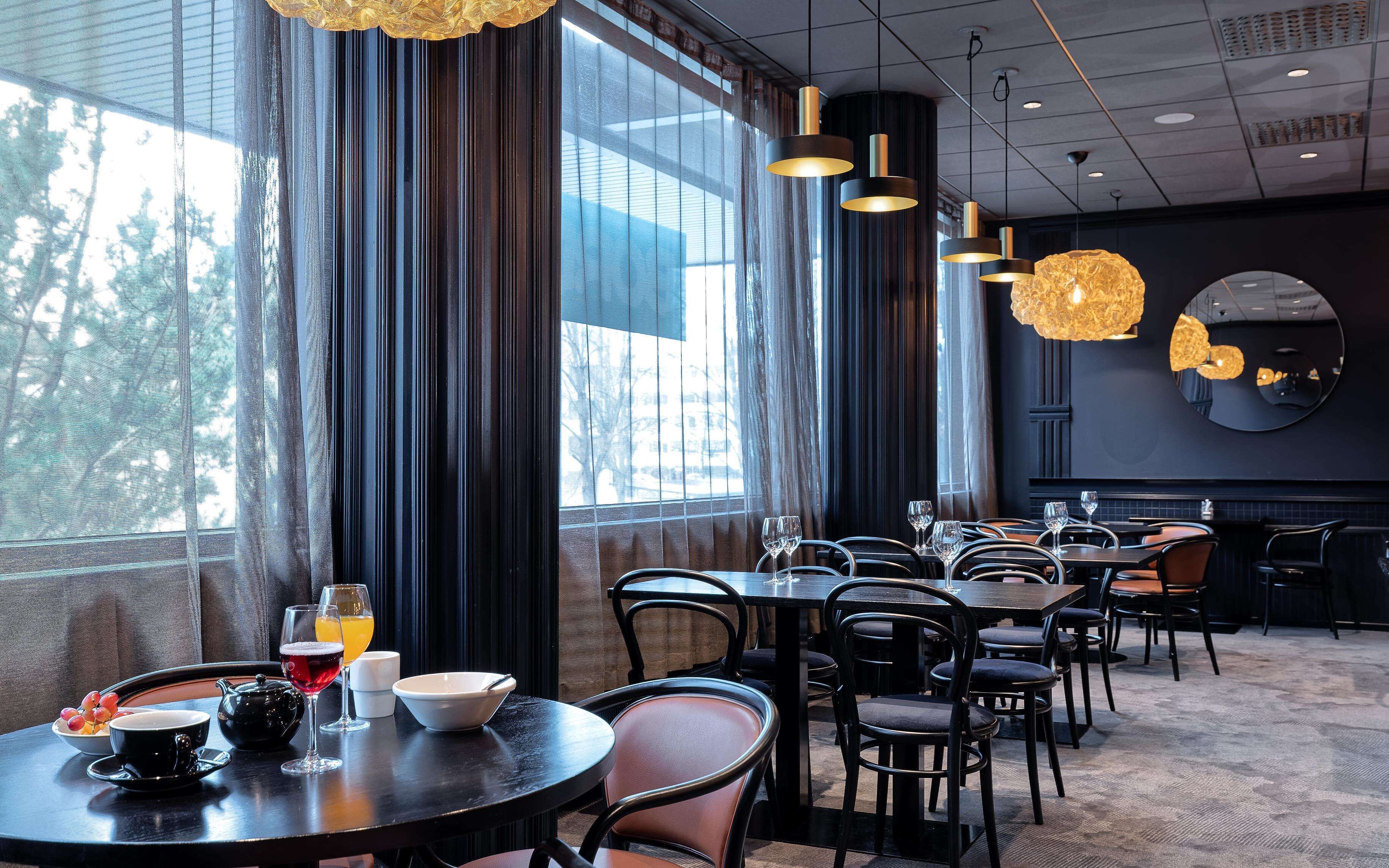 A restaurant with round tables, black chairs, and hanging pendant lights.