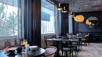 A restaurant with round tables, black chairs, and hanging pendant lights.