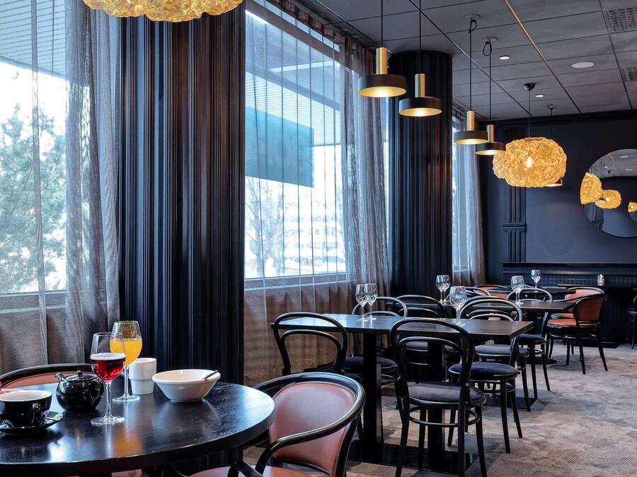 A restaurant with round tables, black chairs, and hanging pendant lights.