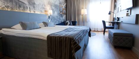 Una habitación de hotel moderna con una cama grande, un escritorio, una silla y un televisor en la pared.