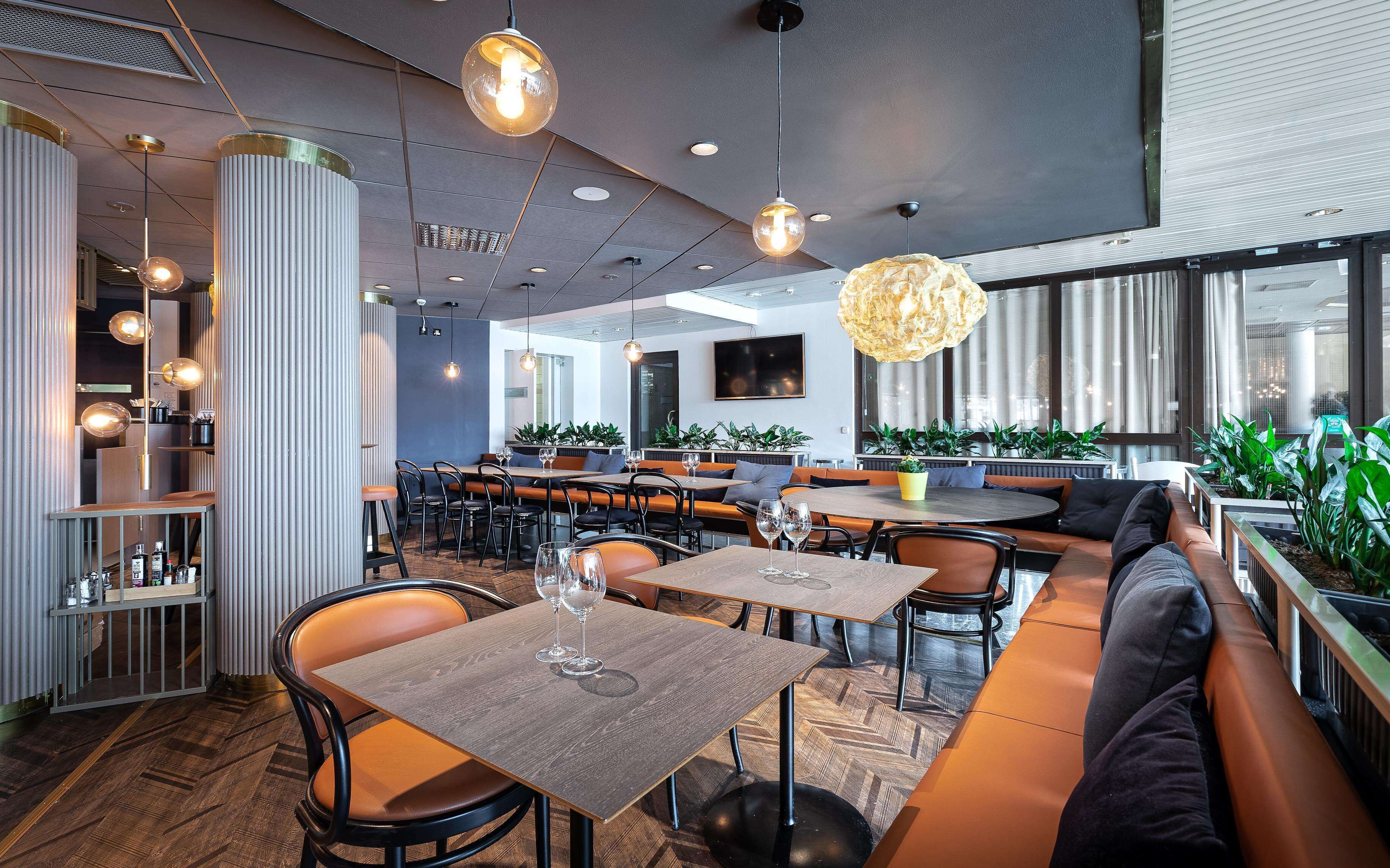 A modern restaurant interior with high tables, booths, and hanging pendant lights.
