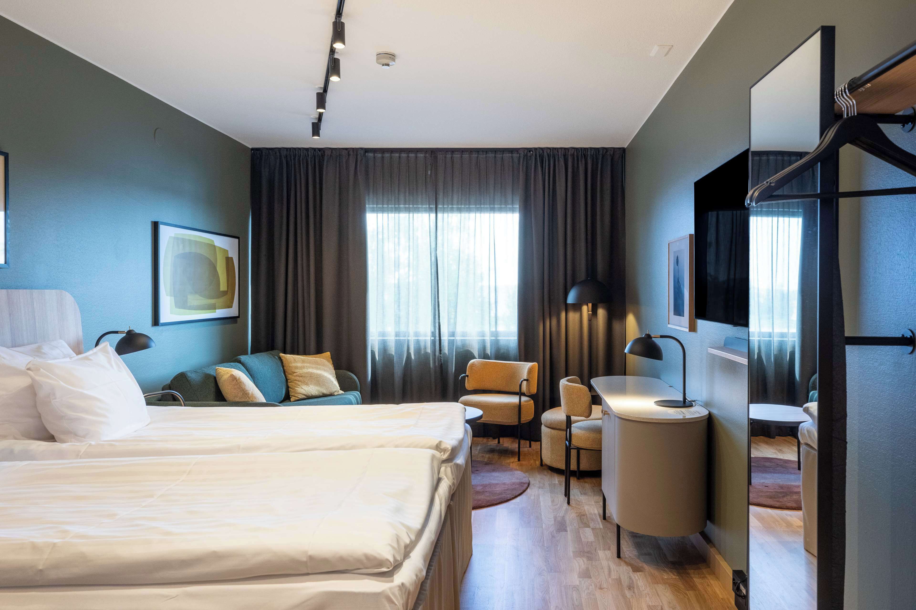 A modern hotel room with a large bed, a desk, a chair, and a TV.
