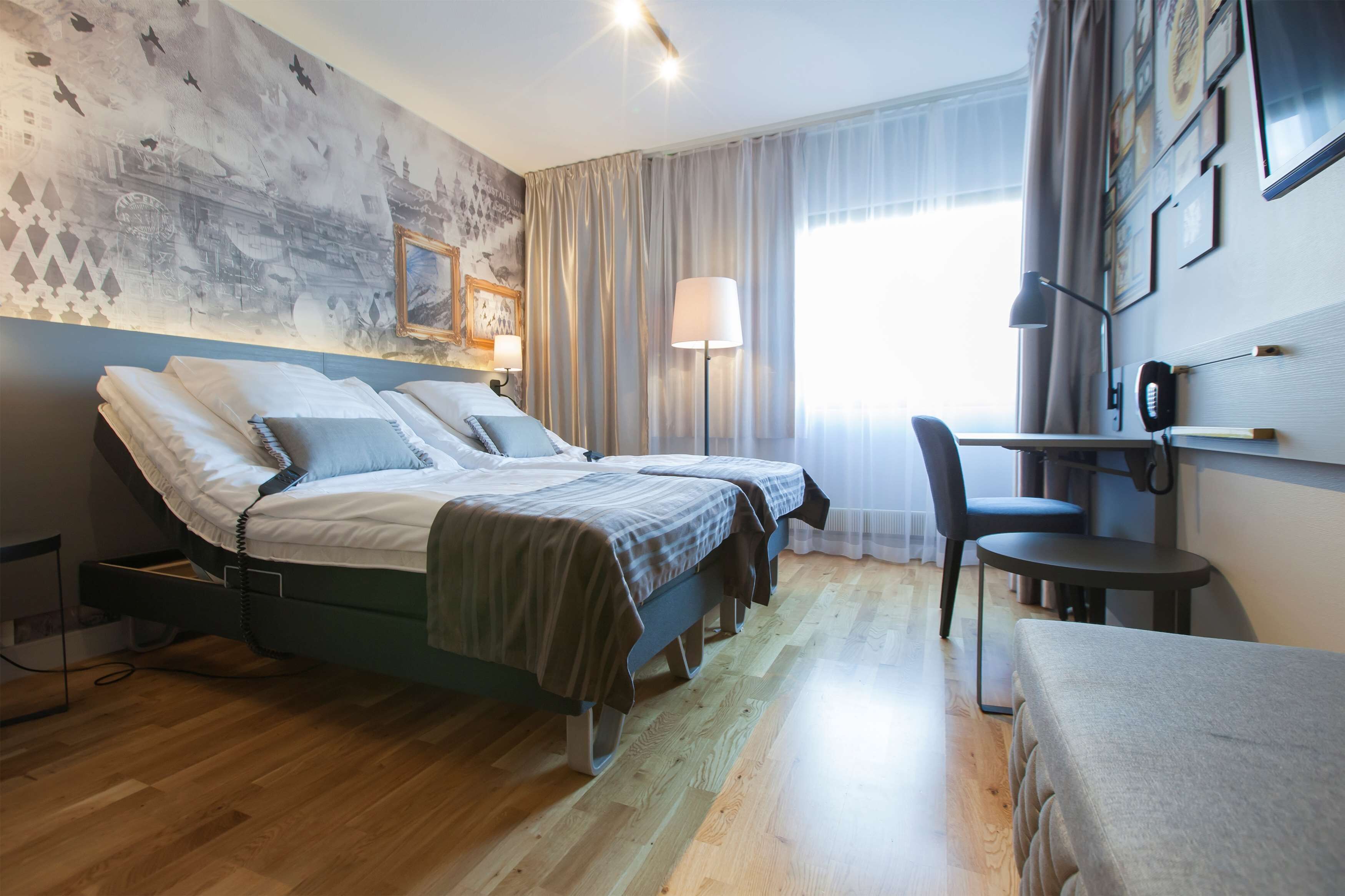 Une chambre d’hôtel moderne équipée d’un lit, d’une table de chevet, d’une lampe et d’un bureau avec une chaise.