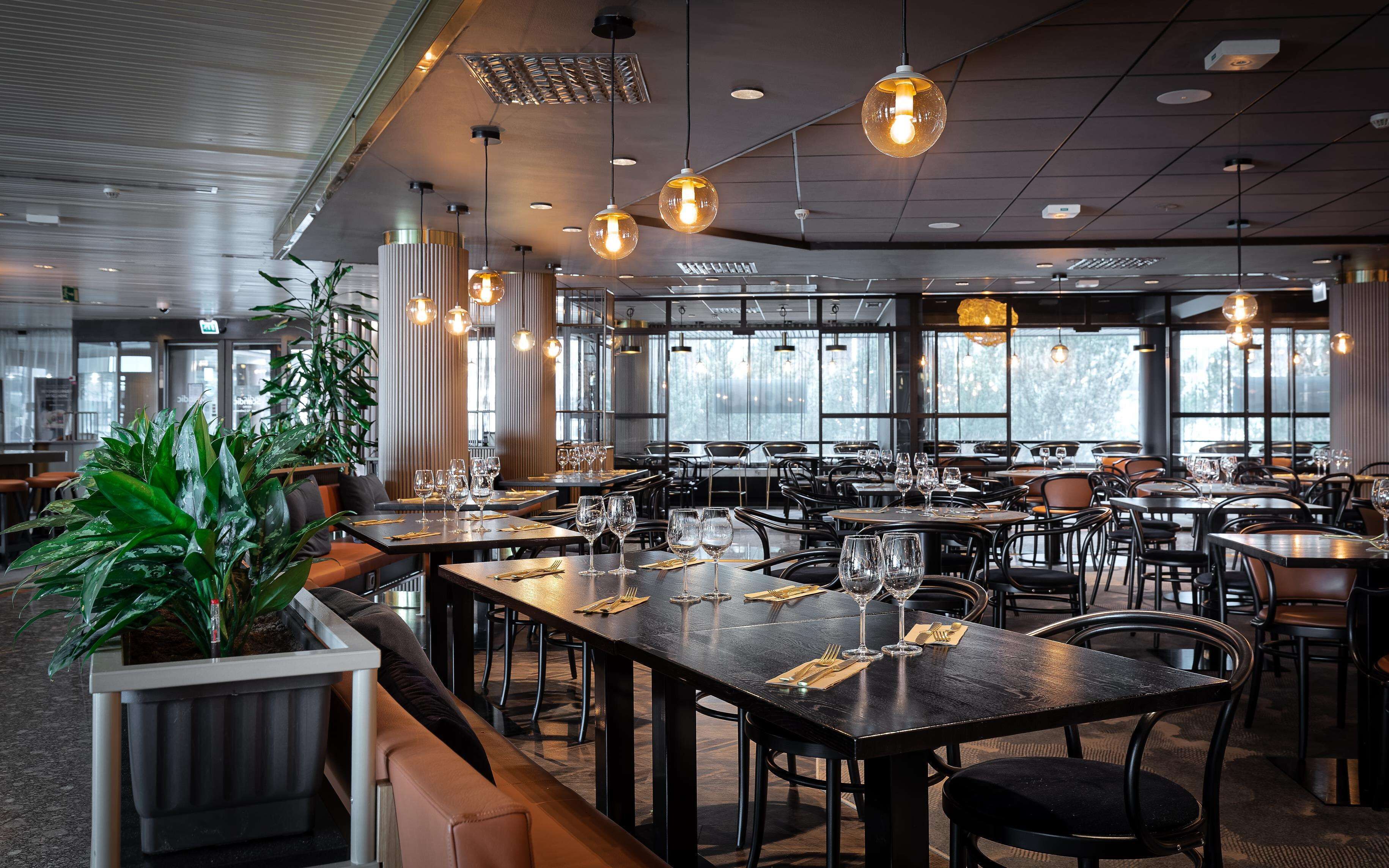 A restaurant with multiple tables, chairs, and hanging pendant lights.