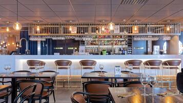 A restaurant with a bar area, multiple tables with chairs, and hanging light fixtures.