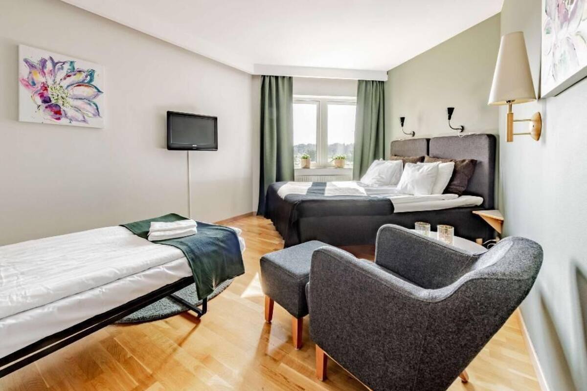 Une chambre d’hôtel avec un lit, un canapé, une télévision et une fenêtre avec des rideaux.