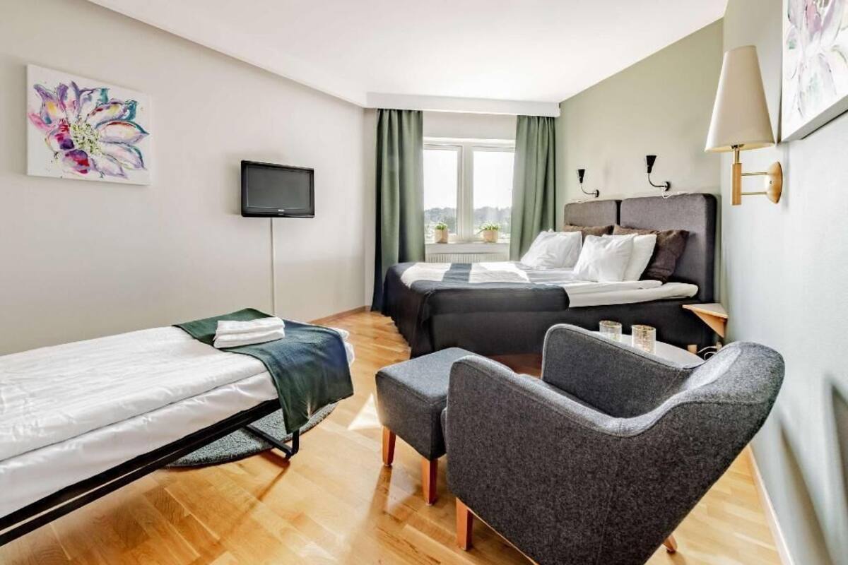 Une chambre d’hôtel avec un lit, un bureau, une chaise, une télévision et une fenêtre avec des rideaux.
