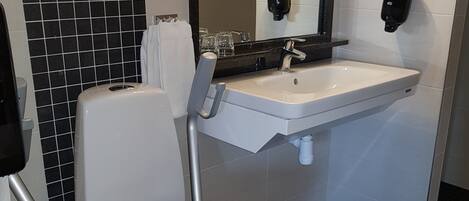 A modern bathroom with a white toilet, black-tiled floor, a white sink, and a mirror above the sink.