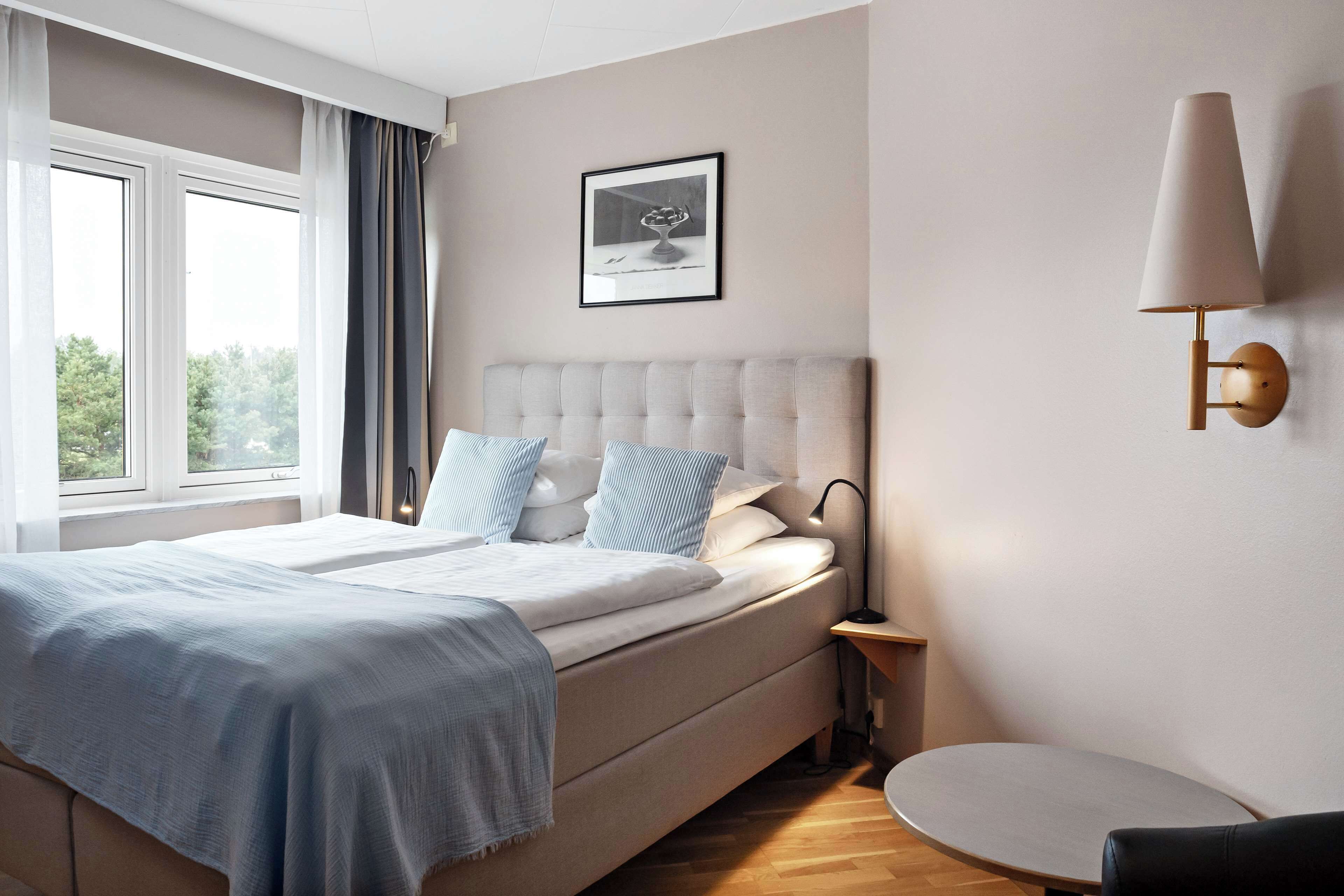 A modern bedroom with a large bed, a bedside table, a lamp, and a framed picture on the wall.