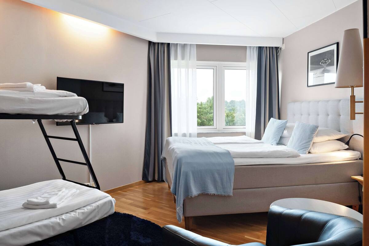 Une chambre d’hôtel moderne équipée d’un lit superposé, d’un téléviseur à écran plat, d’un canapé confortable et offrant une vue sur l’extérieur par la fenêtre.