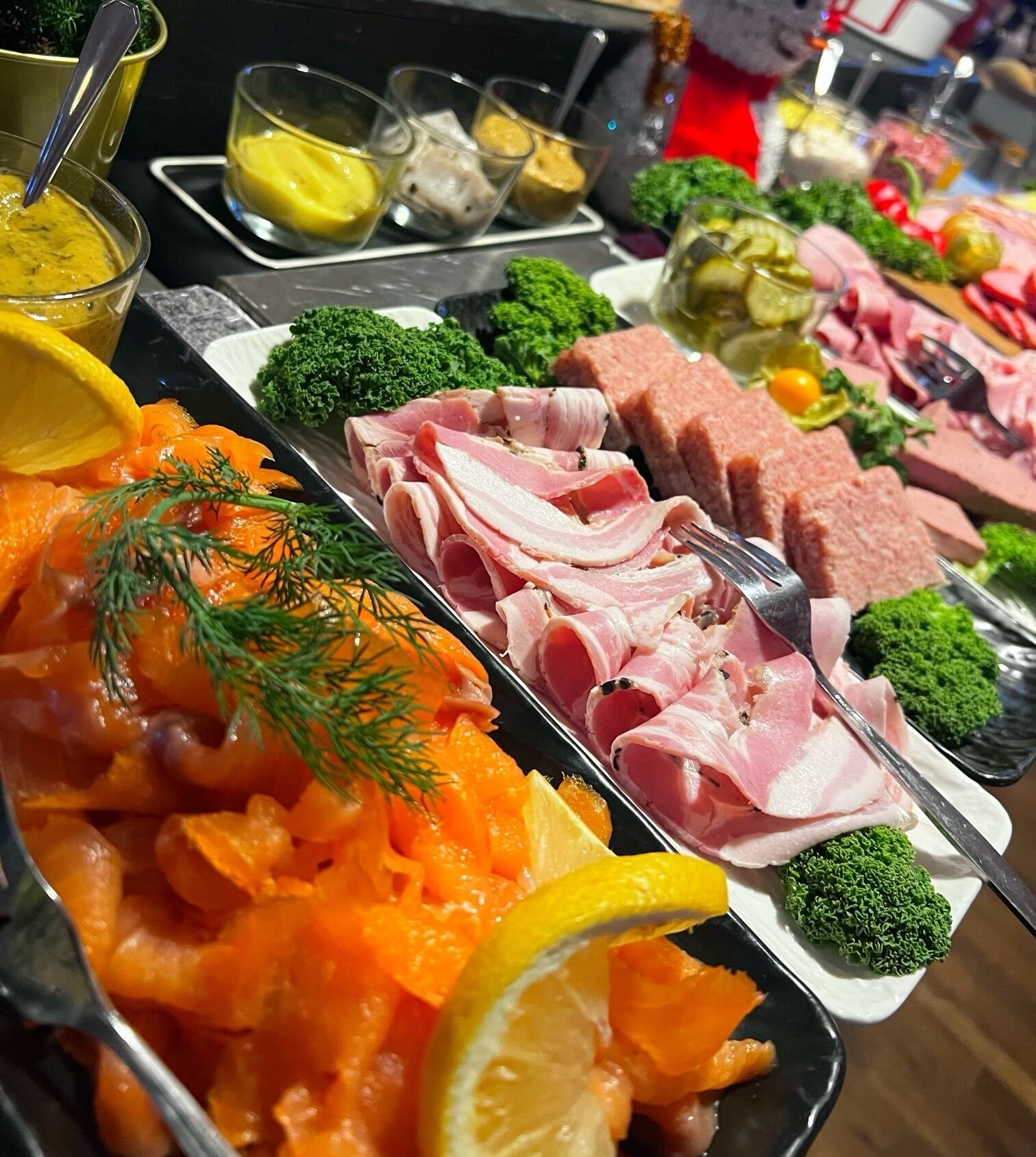 A buffet with various food items including smoked salmon, ham, and pickles.
