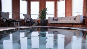 Un área de piscina con piso de vidrio, paredes de madera y un sofá.