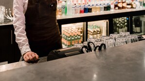 Una camarera en un bar, con una variedad de botellas y vasos en las estanterías detrás de ella.