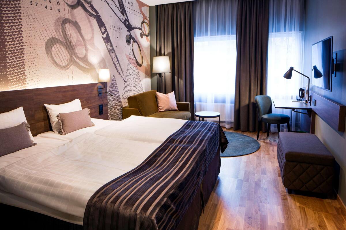 A hotel room with a large bed, a desk with a chair, a sofa, and a TV.