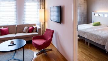 A hotel room with a sofa, a red chair, a bed, a TV, and a lamp.
