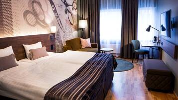 A hotel room with a large bed, a desk with a chair, a small round table, and a sofa.