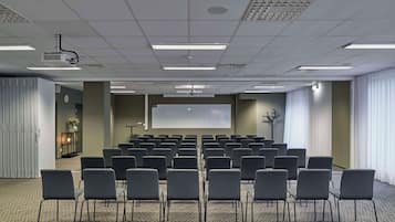 Un salón de conferencias con filas de sillas, un proyector y una pantalla.