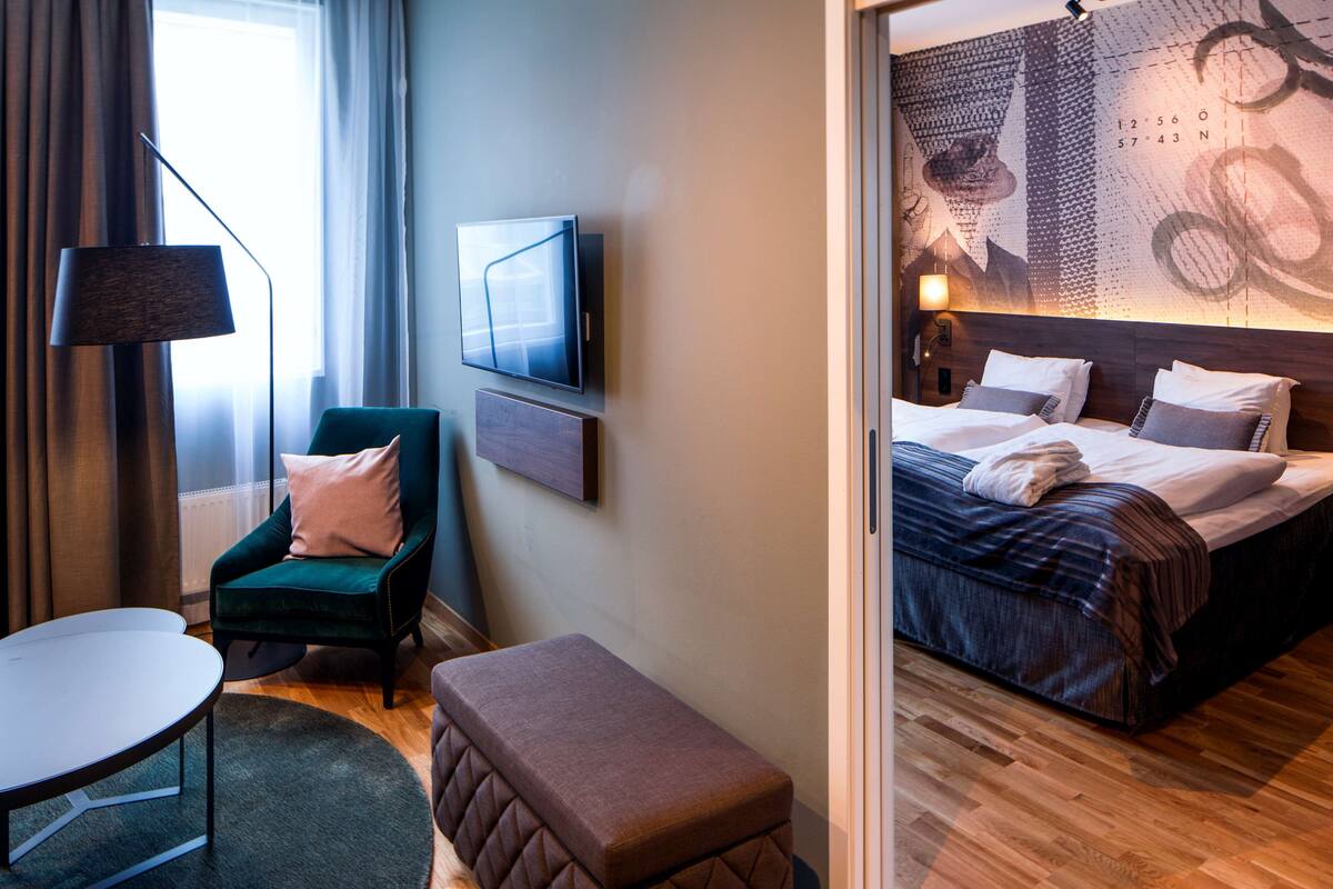 A hotel room with a bed, a chair, a small table, and a wall-mounted TV.