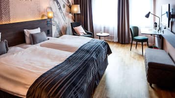 A hotel room with a large bed, two chairs, a desk, and a small table.