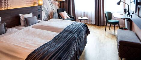 A hotel room with a large bed, two chairs, a desk, and a small table.