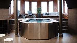 Un área de piscina interior moderna con un jacuzzi, asientos y grandes ventanales.
