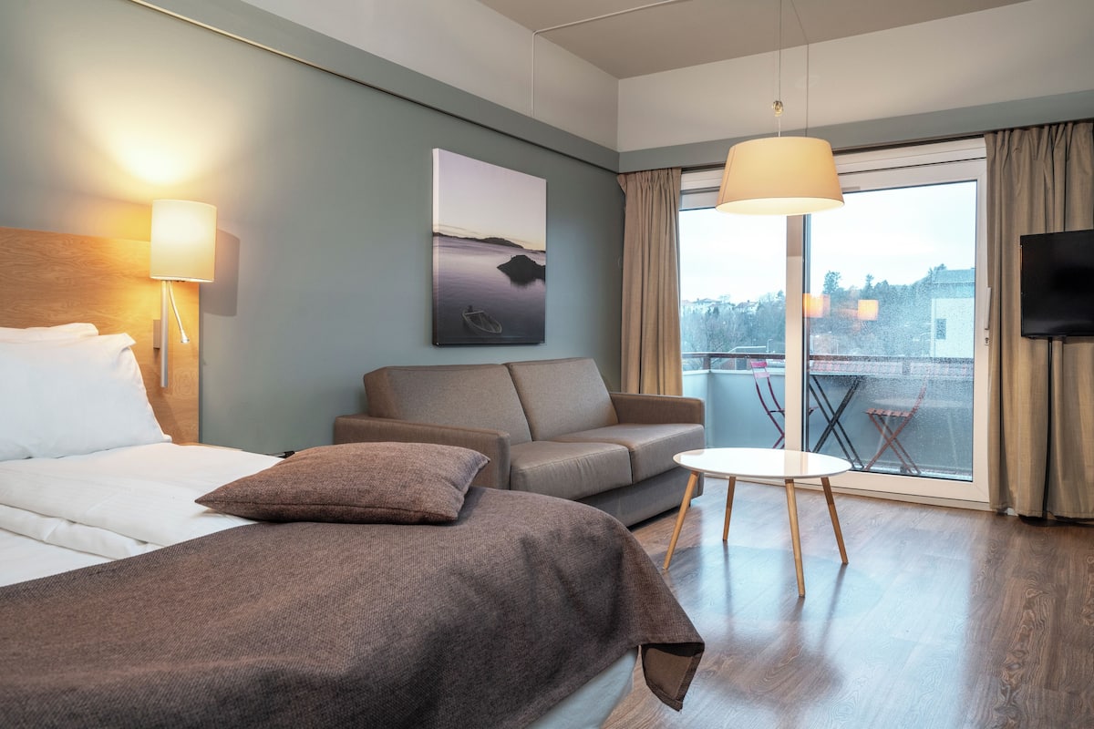 Quarto de hotel com cama, sofá, mesa pequena, televisão e janela com vista.