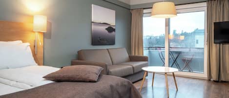 A hotel room with a bed, a sofa, a small table, a TV, and a window with a view.
