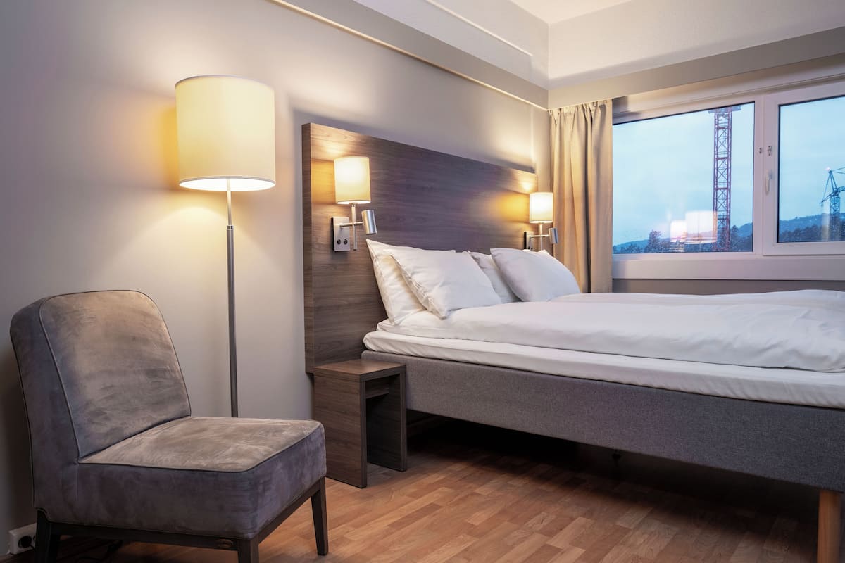 Quarto de hotel com cama, cadeira, mesa de cabeceira e abajur.