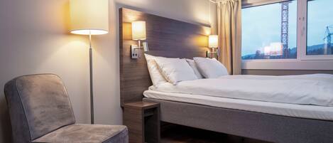 Una habitación de hotel con cama, una silla, una mesita de noche y una lámpara.