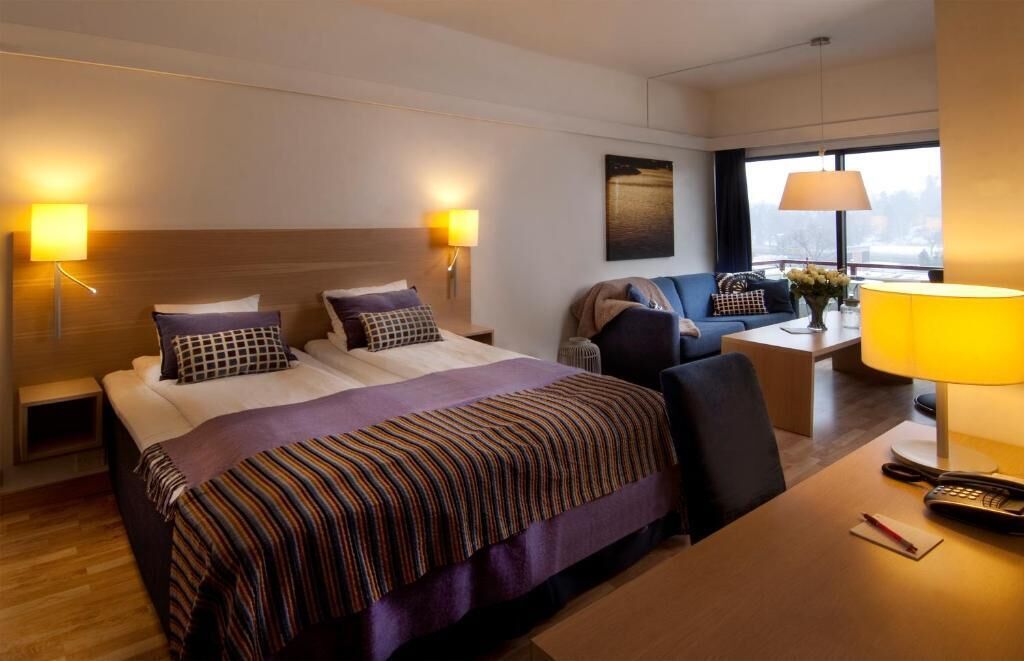 Habitación de hotel con cama, mesitas de noche, escritorio, una silla y vista a la ciudad por la ventana.