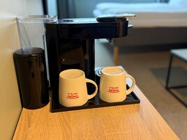Una cafetera con dos tazas blancas sobre una bandeja, un recipiente de vidrio y un objeto negro sobre una superficie de madera.