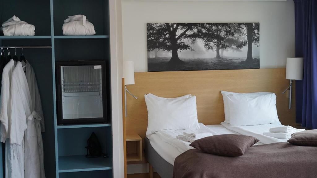 Habitación de hotel con cama, armario, espejo, un cuadro de un árbol y una lámpara.