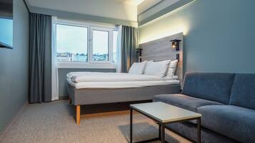 Una habitación de hotel moderna con una cama, un sofá, una mesita y un ventanal con cortinas.