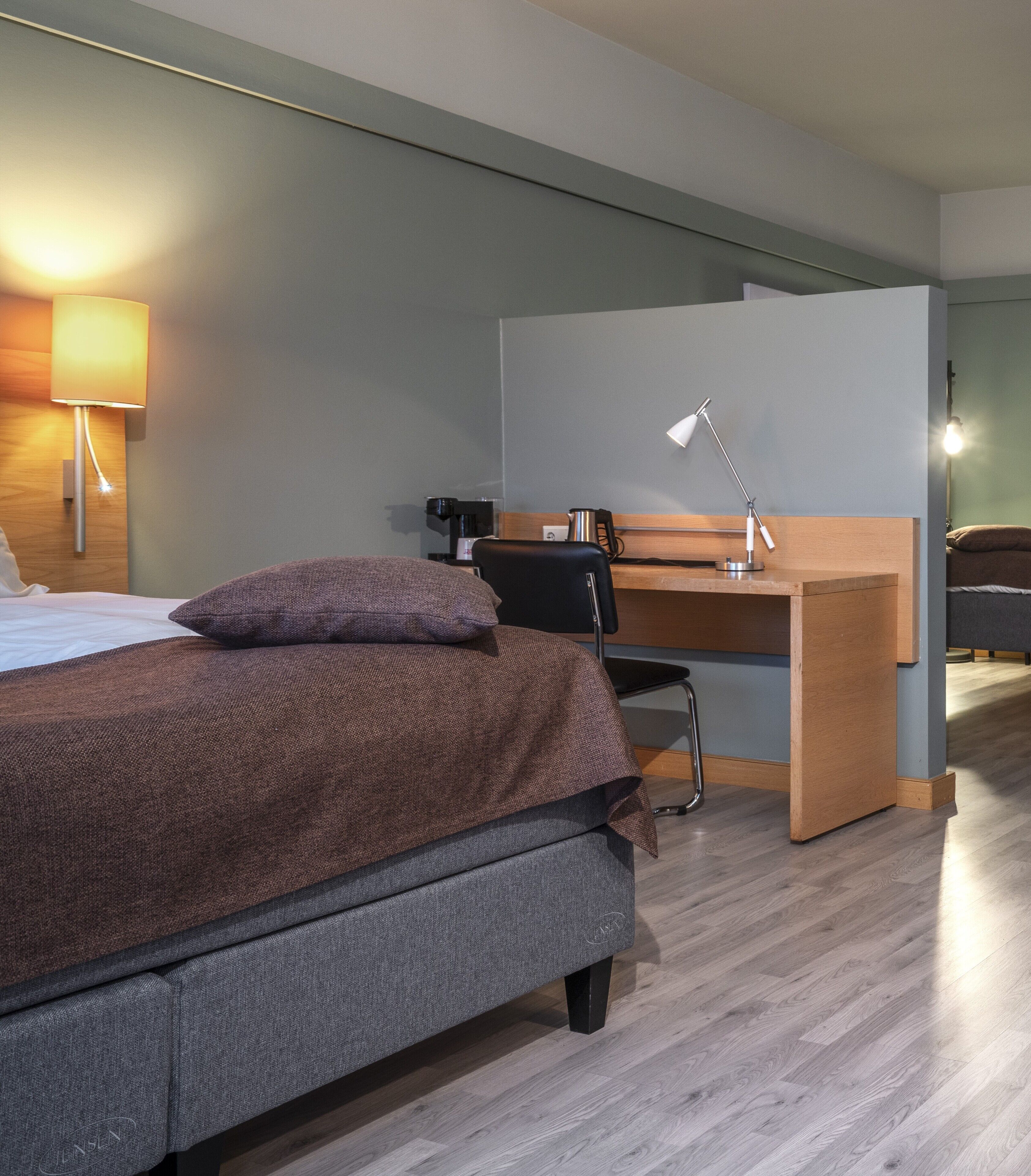 Een moderne hotelkamer met een bed, bureau, stoel, lamp en een koffieapparaat.