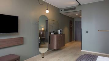 Una camera d'albergo moderna con una televisione a schermo piatto, una testiera di legno, uno specchio grande, un armadio e un letto con copripiumino a righe.
