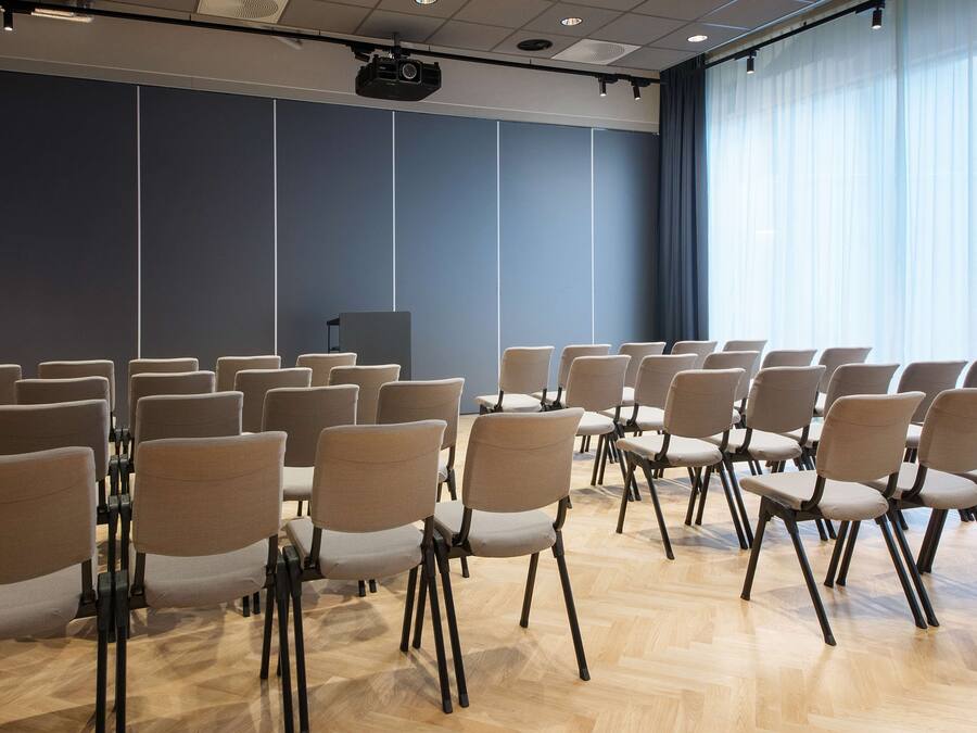 Ett konferensrum med rader av stolar, en talarstol och en stor skärm.