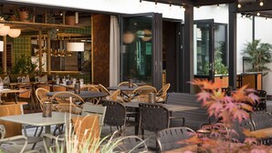 An outdoor dining area with wicker chairs and tables, surrounded by potted plants and a view of the cityscape. - Scandic Sjølyst (Oslo)