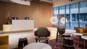 A modern reception area with a wooden panel wall, a reception desk, and a large window offering a view of the city. - Scandic Sjølyst (Oslo)