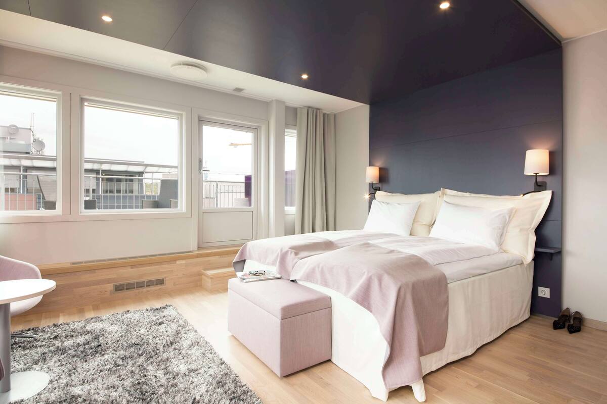 Un dormitorio moderno con una cama grande, una mesita pequeña y vistas a la ciudad.