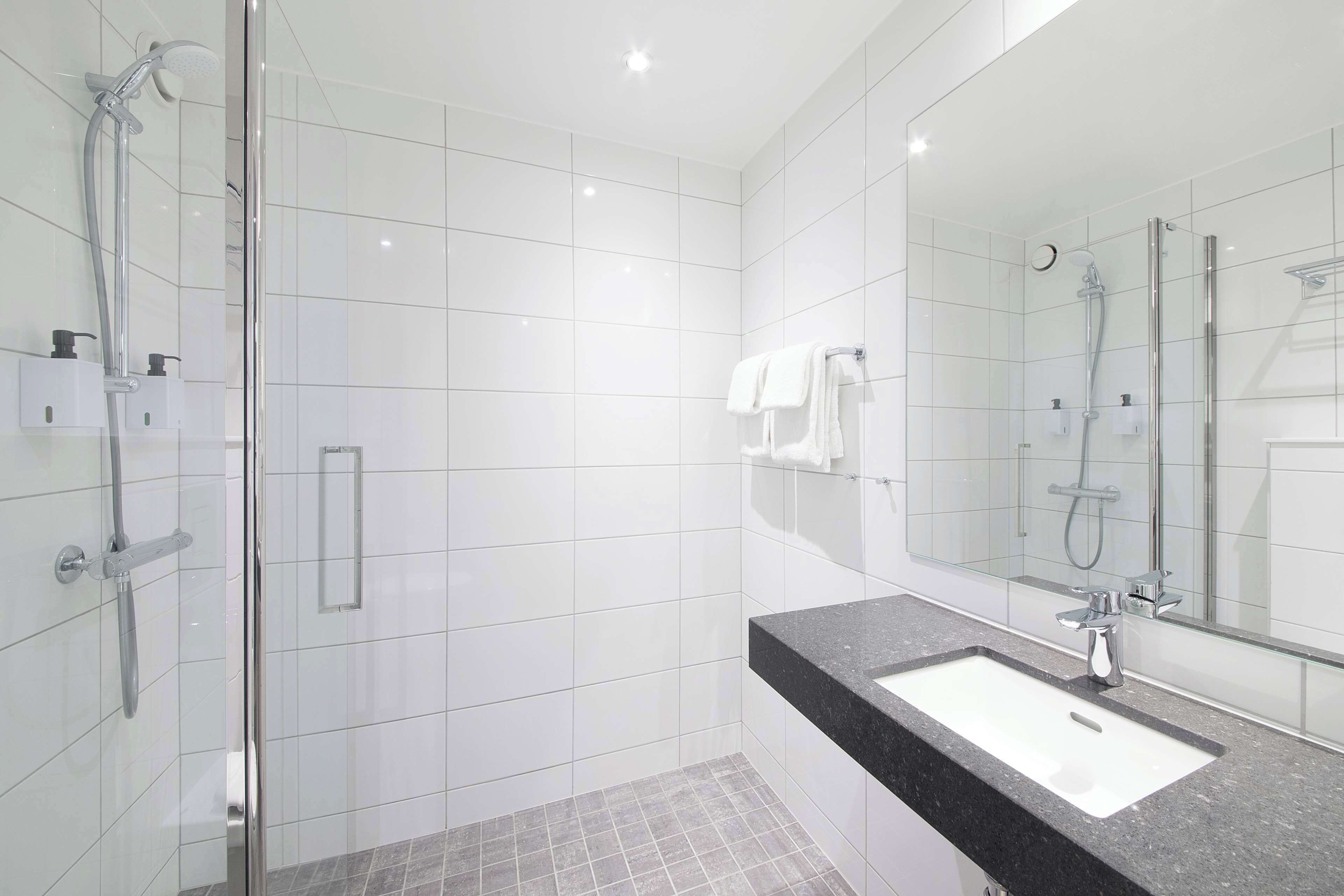 A modern bathroom with a glass-enclosed shower, a black countertop sink, and a large mirror.