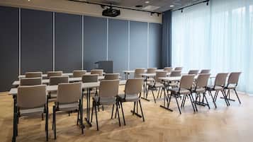 Un salón de conferencias con varias mesas y sillas, un proyector y un amplio ventanal con cortinas.