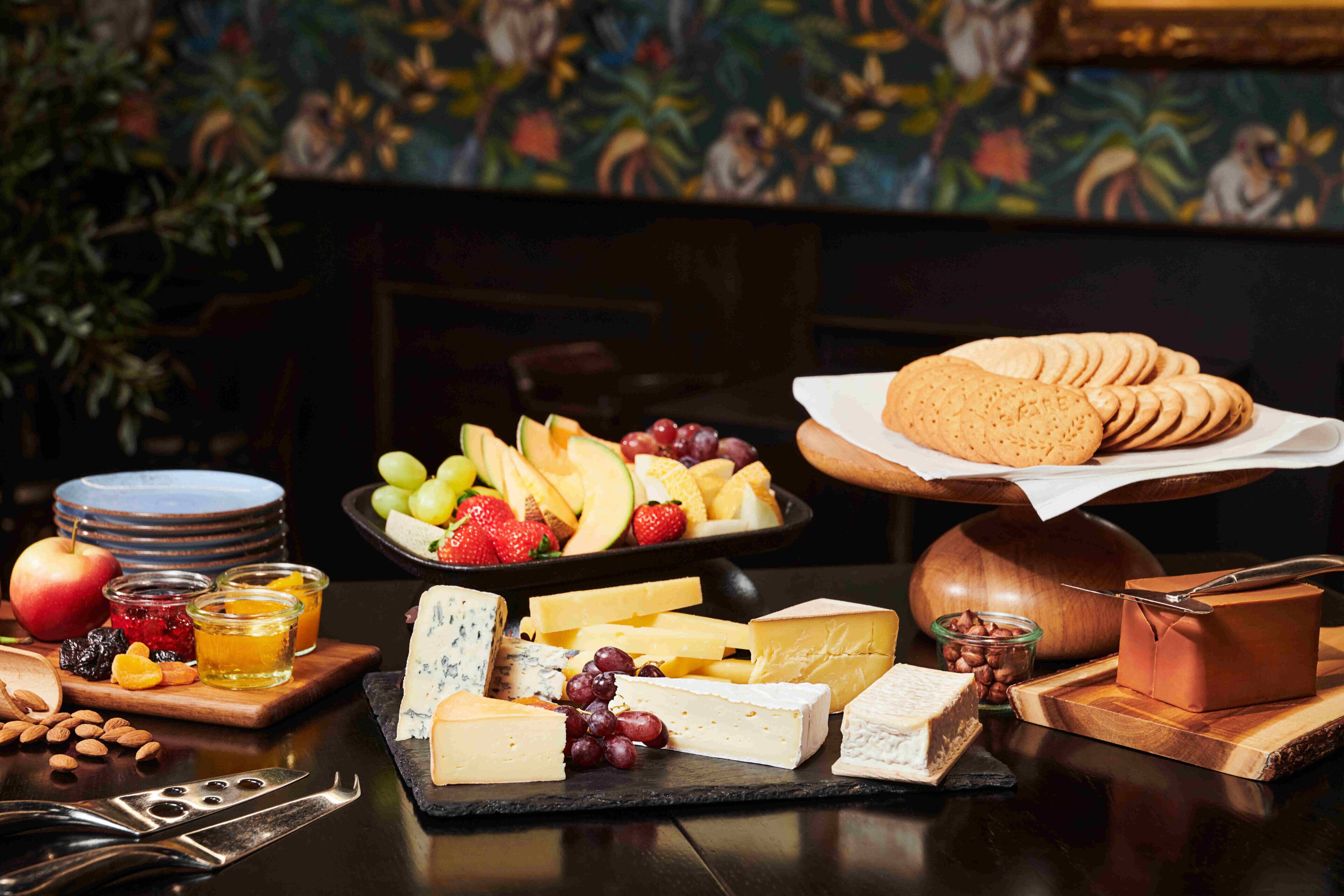A variety of cheeses, fruits, and nuts on a wooden table with a decorative background.