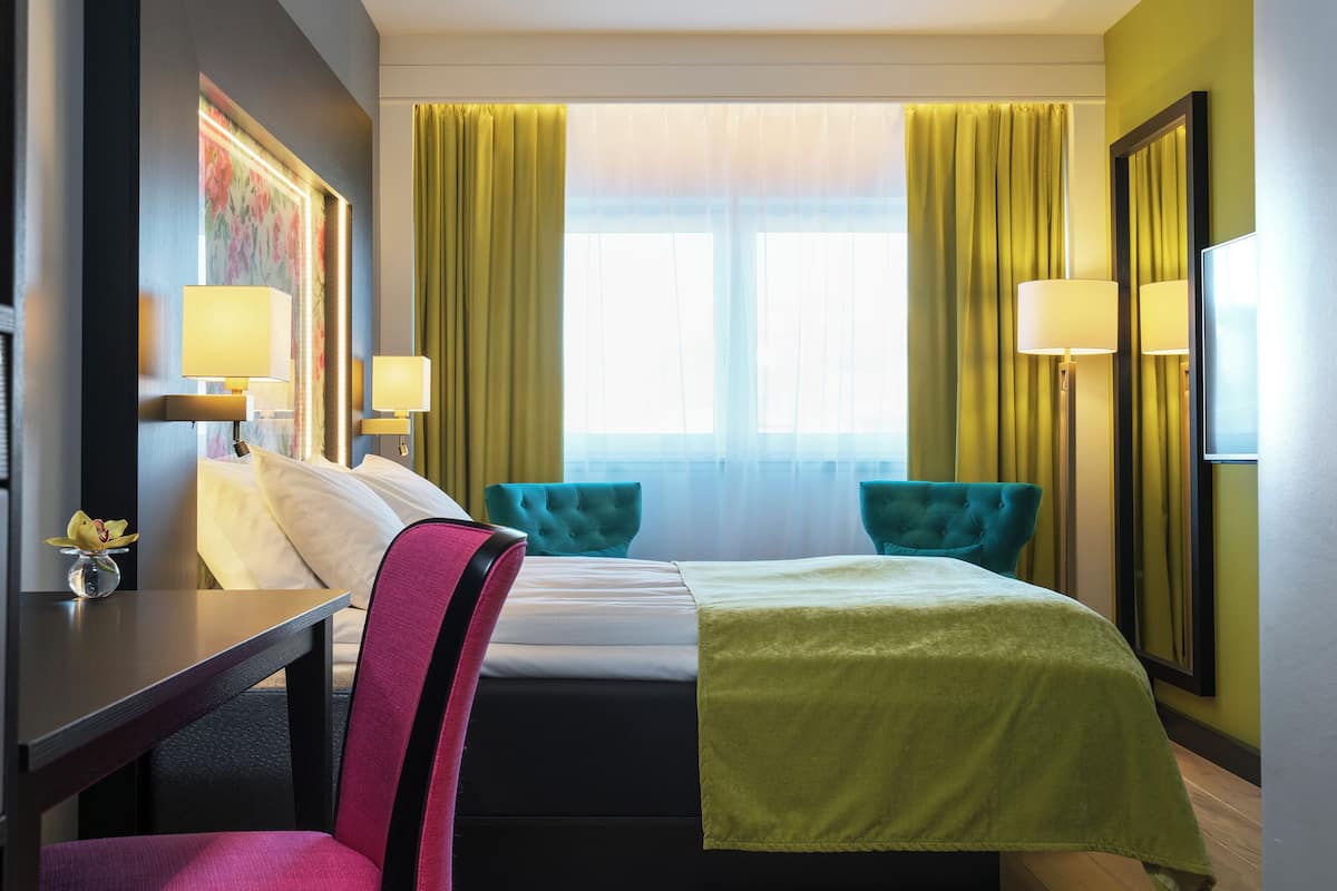 Una habitación de hotel con una cama, dos sillas, un escritorio y una lámpara.