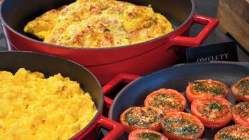 Une cuisine avec trois casseroles contenant des œufs brouillés, une frittata et des tomates au four.